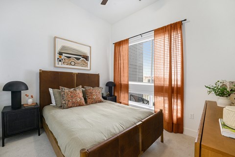 A bedroom with a bed, nightstand, and window with curtains.