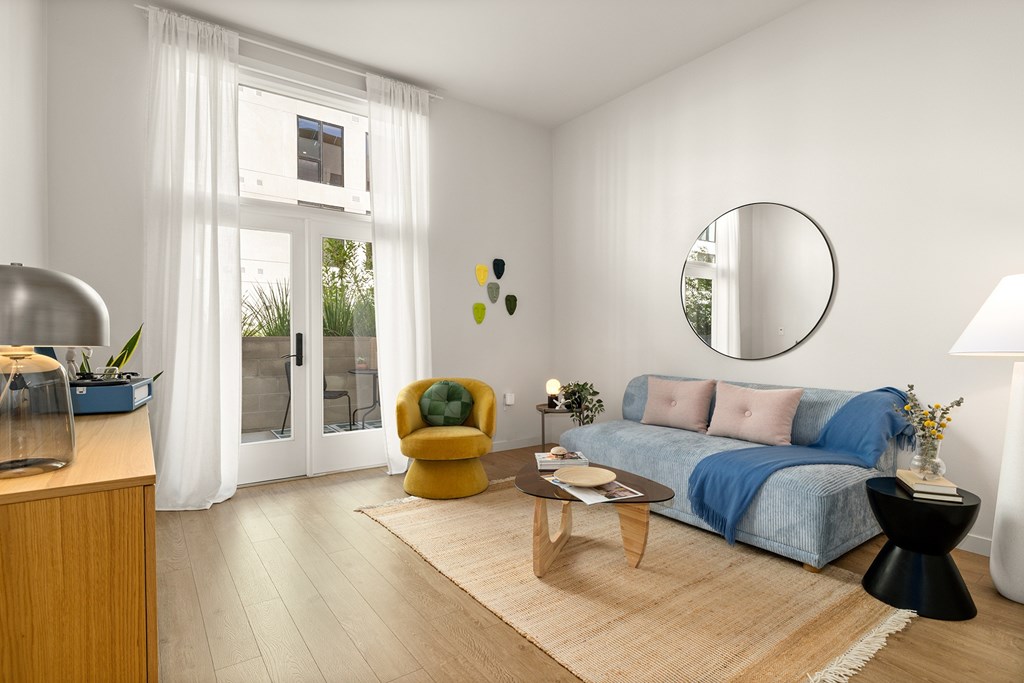 A modern living room with a blue sofa, yellow chair, and a round mirror on the wall.