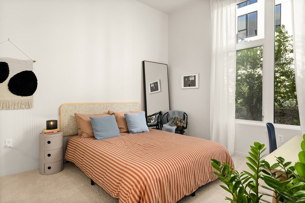 A bedroom with a bed, nightstand, and a plant.