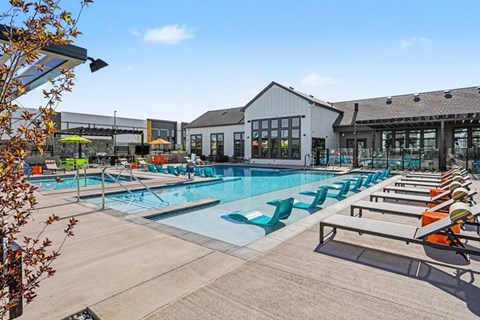 A large outdoor swimming pool with lounge chairs and a building in the background.