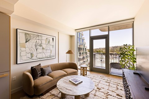 A living room with a couch, a coffee table, and a large window overlooking a balcony.