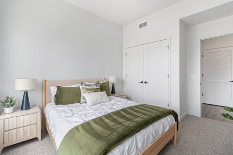 A bedroom with a bed, nightstand, and a plant.