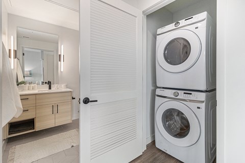 A white washing machine is stacked on top of another white washing machine in a small laundry room.