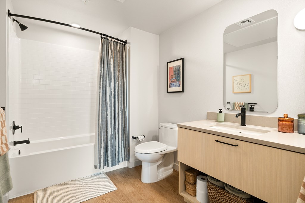 A bathroom with a white toilet, a white sink, and a white bathtub with a grey shower curtain.