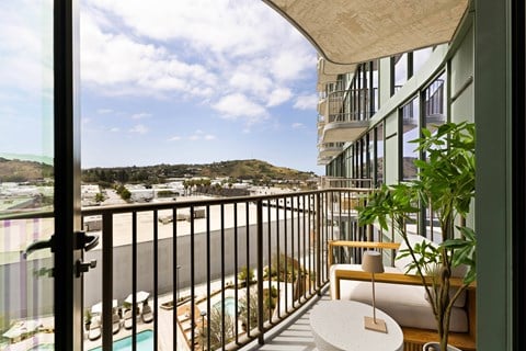 A balcony with a table and chairs overlooking a pool and a hillside.
