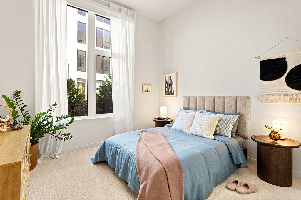 A bedroom with a large bed and a window with white curtains.