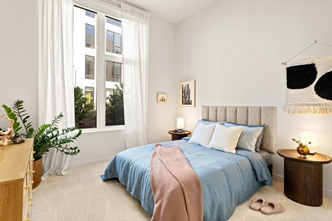 A bedroom with a large bed and a window with white curtains.