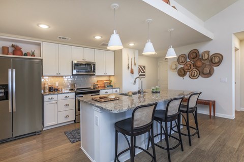 a kitchen with an island with four chairs and a stainless steel refrigerator