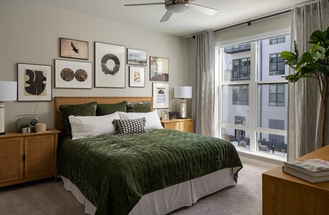A bedroom with a bed, a ceiling fan, and a window with a view of a building outside.