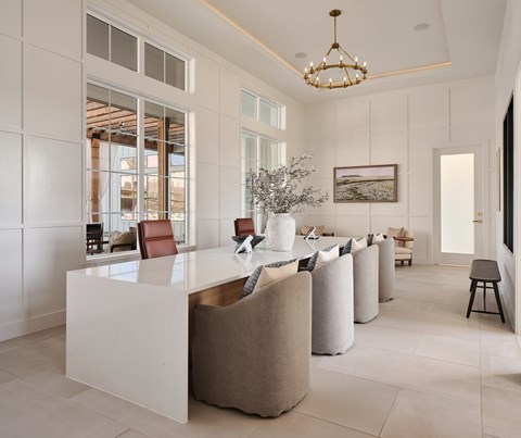 A white reception desk with a gold top is surrounded by beige chairs in a spacious room.