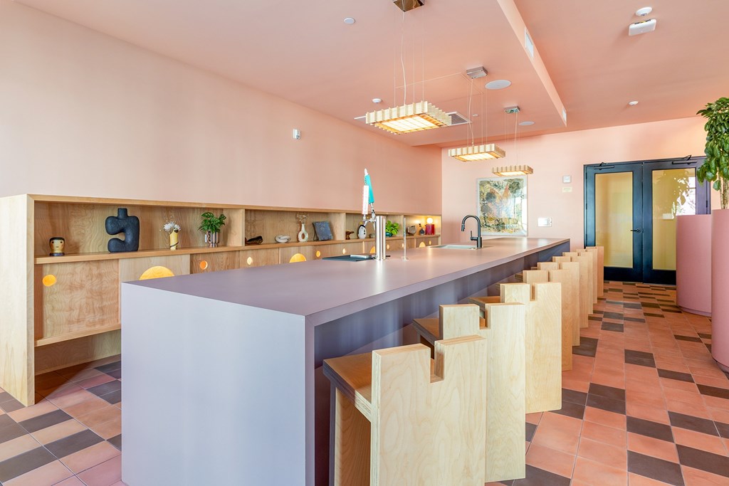 A long white table is in the middle of a room with pink walls.