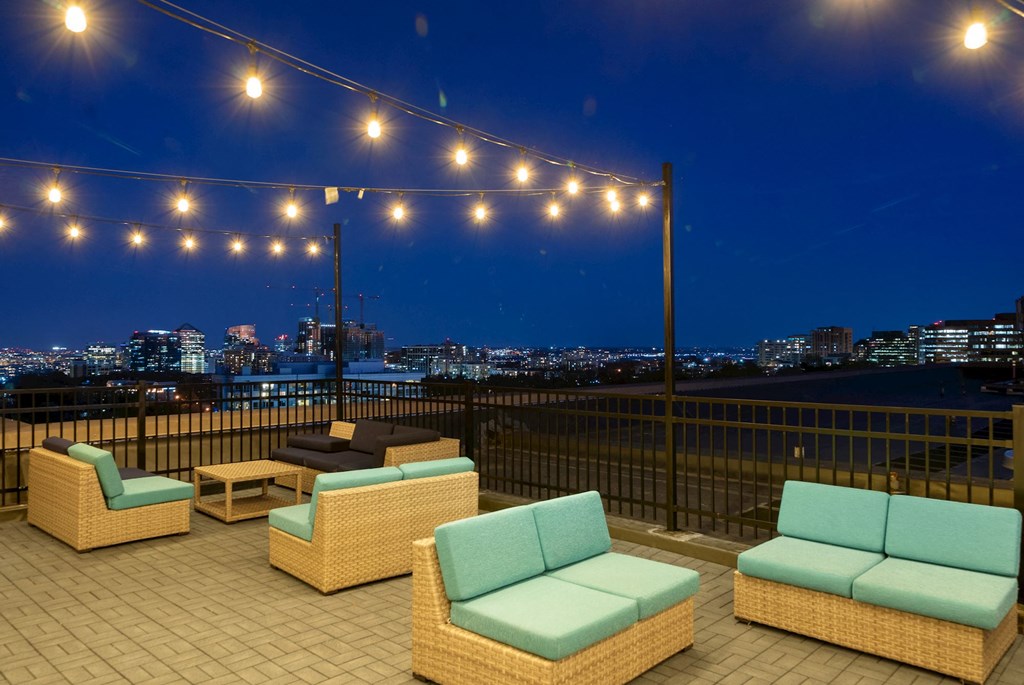 a rooftop deck with chairs and a view of the city at night