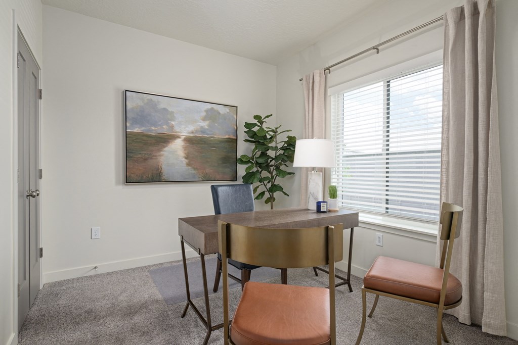 Office room area with a painting on the wall, a table with chairs, and a potted plant.