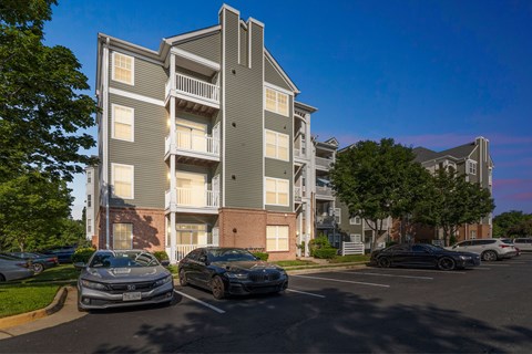 A grey apartment building with cars parked in front.