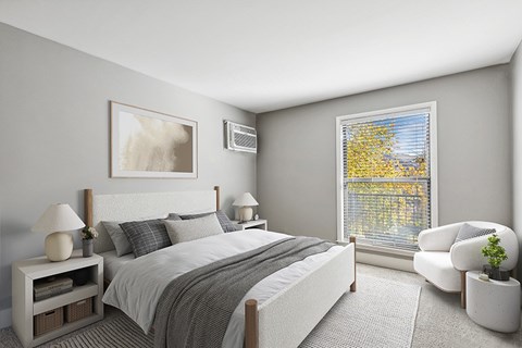 A bedroom with a large bed, a nightstand with a lamp, a chair, and a window with a view of trees outside.