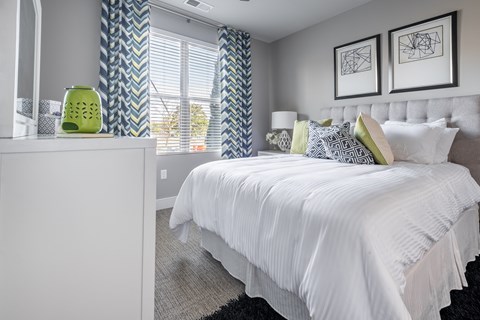 A bedroom with a white bed and a green vase on a nightstand.