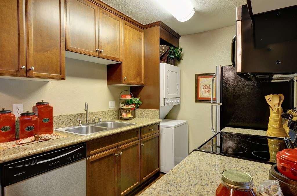 A kitchen with wooden cabinets and in unit washer and dryer.