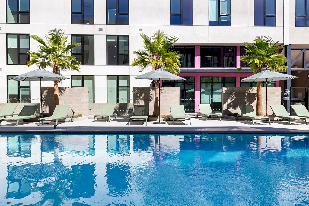 A pool with lounge chairs and umbrellas in front of a multi-story building.
