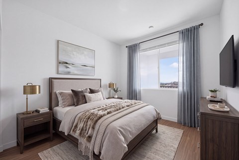 A bedroom with a large bed, a nightstand with a lamp, a dresser, and a window with curtains.