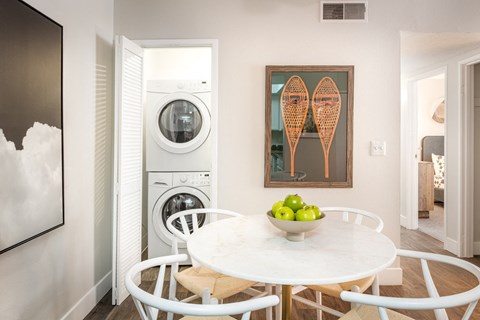 a dining room with a white table and chairs and a washing machine in a kitchen