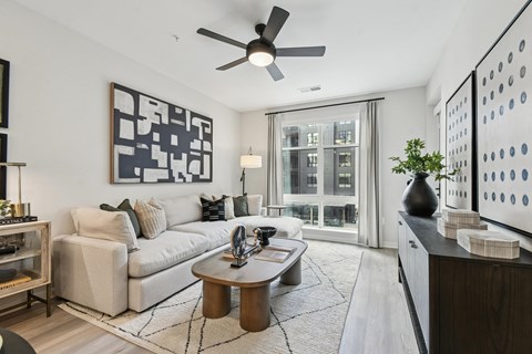A modern living room with a white sofa, a wooden coffee table, and a large abstract painting on the wall.