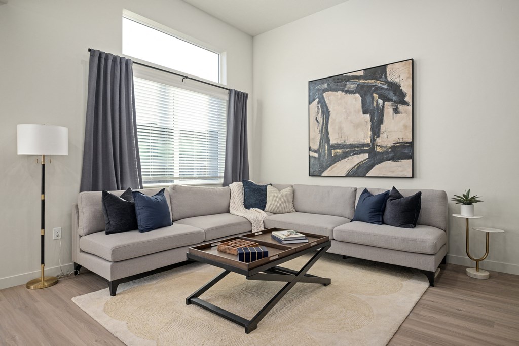 A living room with a grey couch, a coffee table, and a painting on the wall.