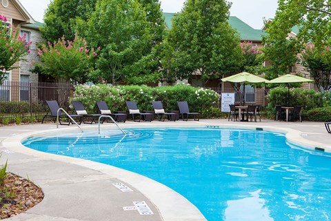 A pool surrounded by trees and chairs.