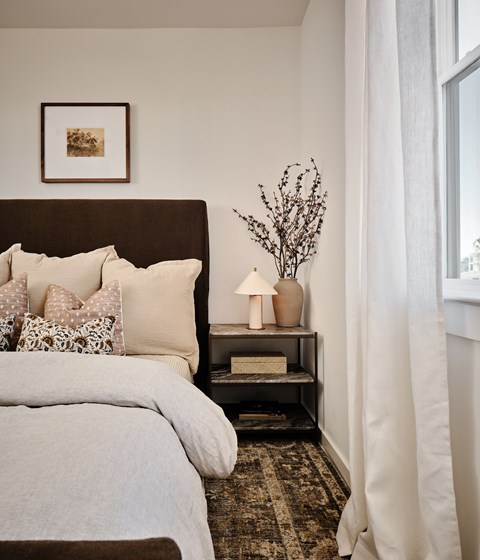 A bedroom with a large bed and a nightstand with a lamp and vase.