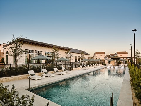 A pool with a waterfall and lounge chairs in front of a building.