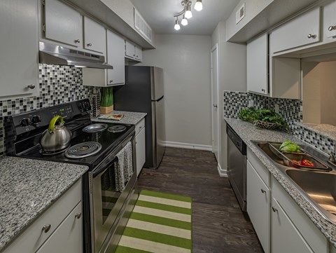 A kitchen with a black refrigerator and a green and white striped rug.