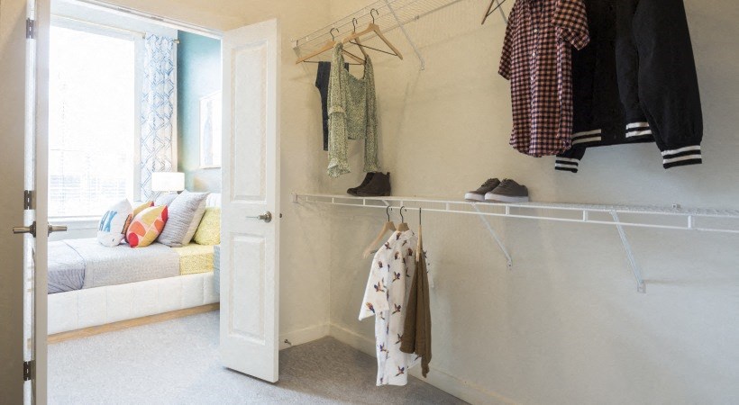 a closet with clothes hanging on a rack and a door to a bedroom