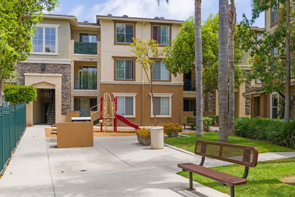 A brown bench sits on a sidewalk in front of a building.
