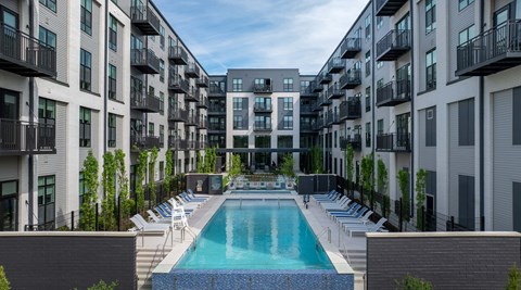 A swimming pool is surrounded by lounge chairs and apartment buildings.