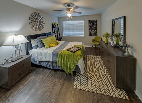A bedroom with a bed, dresser, and mirror. Un dormitorio con una cama, una cómoda y un espejo.