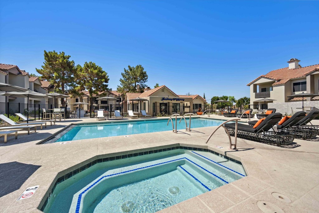 A large outdoor swimming pool surrounded by lounge chairs and buildings.