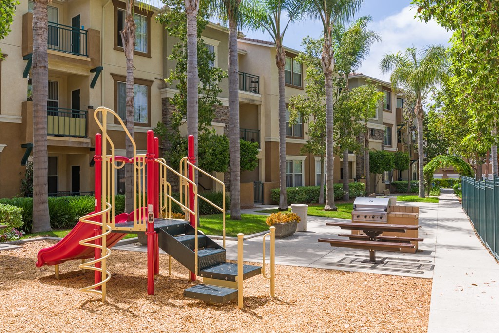 A playground with a red slide and a yellow slide in front of apartment buildings.