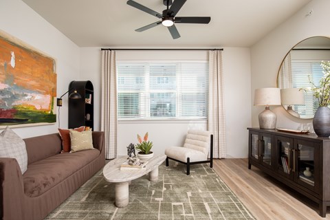 A living room with a brown couch, a white chair, a coffee table, and a painting on the wall.