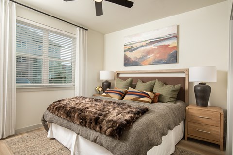 A bedroom with a bed, a ceiling fan, and a painting on the wall.