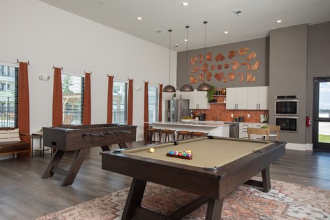 A pool table is in the middle of a room with a kitchen in the background.