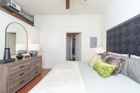 A bedroom with a white bed and a wooden dresser with a mirror.