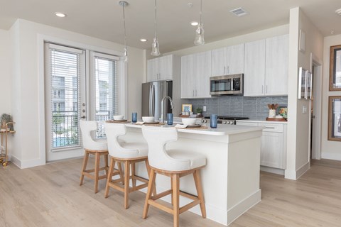 A kitchen with white cabinets and a white island with bar stools.