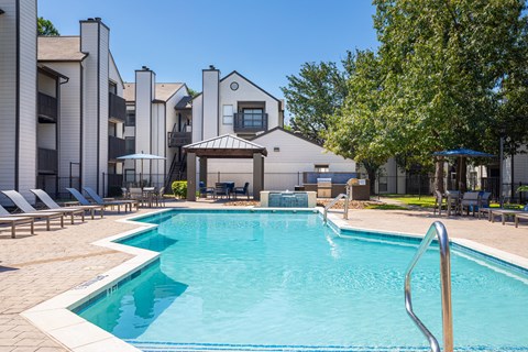 A swimming pool surrounded by lounge chairs and umbrellas in front of a building.