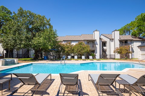 A pool surrounded by lounge chairs and trees.