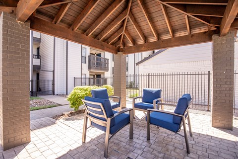 Two blue chairs are under a wooden pergola.