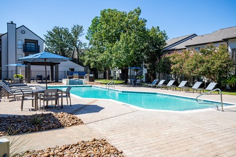 A pool surrounded by chairs and trees.