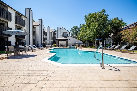 A swimming pool surrounded by lounge chairs and umbrellas in a sunny outdoor setting.