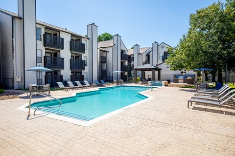 A swimming pool surrounded by lounge chairs and umbrellas in front of apartment buildings.