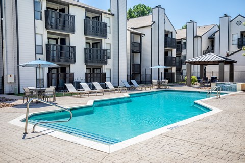 A swimming pool surrounded by lounge chairs and umbrellas in front of apartment buildings.