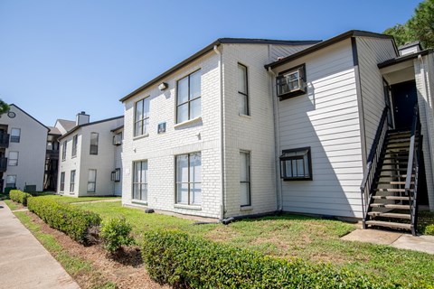 A white two-story apartment building with a staircase leading to the second floor.