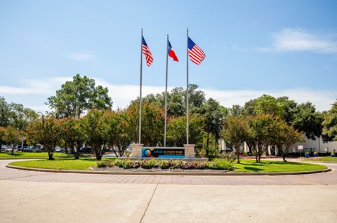 Two American flags are flying in front of a sign with a circular logo.